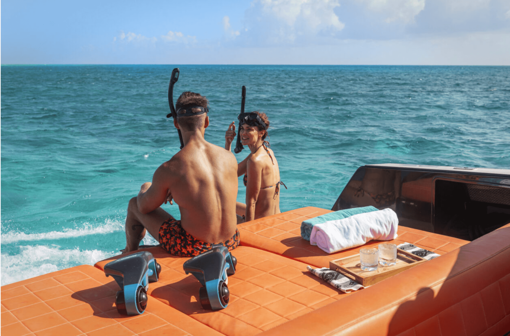 couple with snorkels on sit at end of boat to jump in water